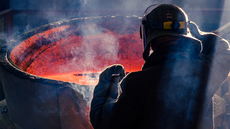 Steelworker stirs mixture at hot cauldron
